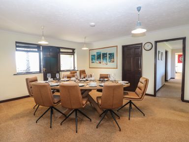A dining room with a large wooden table surrounded by ten brown chairs at Beach Haven in Happisburgh East Anglia