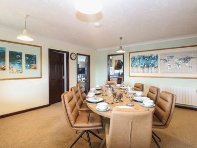 A dining room with a wooden table set with plates bowls and glasses surrounded by brown chairs at Beach Haven in Happisburgh East Anglia