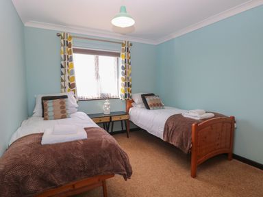 A bedroom with two single beds a small table and window with patterned curtains at Beach Haven in Happisburgh East Anglia