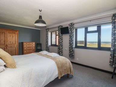 A bedroom with a bed towel sets windows showing sea view wooden wardrobe and chest of drawers at Beach Haven in Happisburgh East Anglia