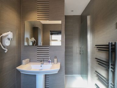 A bathroom with a sink and mirror next to a glass shower door with tiled walls at Beach Haven in Happisburgh East Anglia