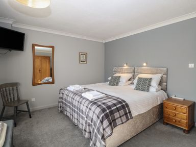 A bedroom with a double bed wooden nightstand wall mirror chair and mounted television at Beach Haven in Happisburgh East Anglia