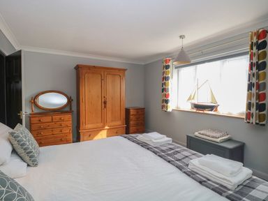 A bedroom with a bed folded towels wooden furniture and a model sailboat on the windowsill at Beach Haven in Happisburgh East Anglia