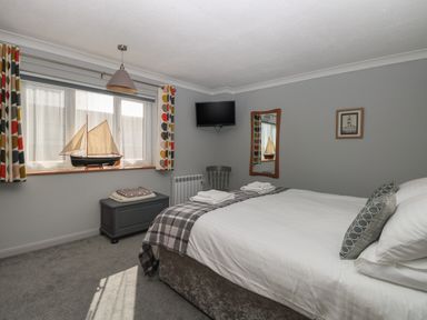 A bedroom with a bed pillows a wall-mounted TV a mirror framed picture and a window with patterned curtains at Beach Haven in Happisburgh East Anglia
