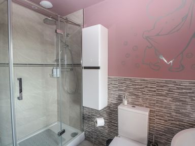 A bathroom with a glass shower enclosure a white wall cabinet and a toilet at Beach Haven in Happisburgh East Anglia