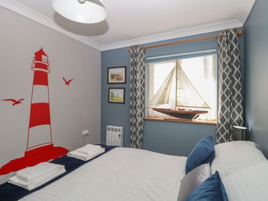 A bedroom with a bed and towels by a window with a model sailboat and lighthouse wall art at Beach Haven in Happisburgh East Anglia