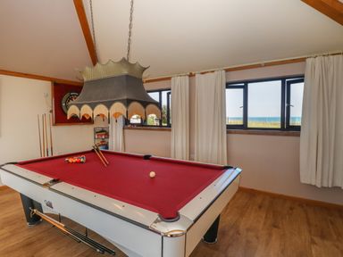 A game room with a red pool table wooden floor and windows with curtains at Beach Haven in Happisburgh East Anglia