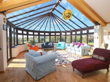 A sunroom with a glass ceiling and multiple chairs and sofas around a colorful rug at Beach Haven in Happisburgh East Anglia