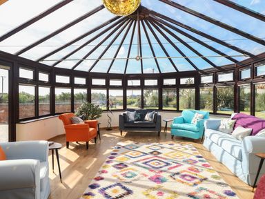 A sunroom with colorful armchairs sofas and a patterned rug at Beach Haven in Happisburgh East Anglia