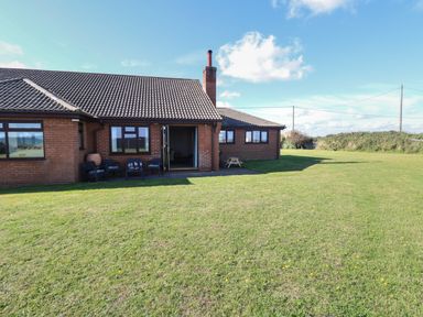 A brick house with a tiled roof and open patio doors overlooking a large grassy lawn at Beach Haven in Happisburgh East Anglia