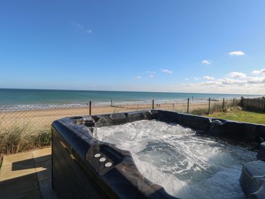 A bubbling hot tub with a view of a sandy beach and ocean at Beach Haven in Happisburgh East Anglia