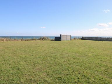 A grassy yard with a hot tub near a fence overlooking the sea at Beach Haven in Happisburgh East Anglia