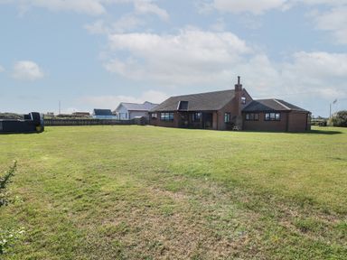 A large grassy yard with a brick house and a small white house in the background at Beach Haven in Happisburgh East Anglia
