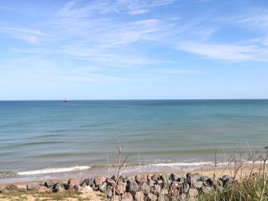A beach with rocks in the foreground and a ship on the horizon in the sea at Beach Haven in Happisburgh East Anglia