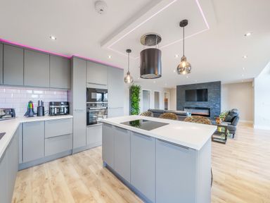 A modern kitchen with an island and built-in appliances connected to a living area with a wall-mounted TV at Micklemore Lakes and Lodges in North Thoresby