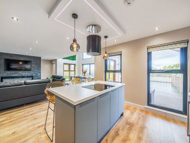 A kitchen island with stools a living room with a TV and a dining area with large windows at Micklemore Lakes and Lodges in North Thoresby