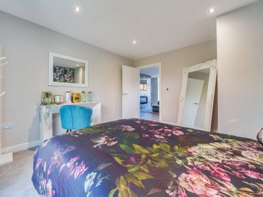 A bedroom with a floral bedspread a blue chair a white desk and a large mirror at Micklemore Lakes and Lodges in North Thoresby