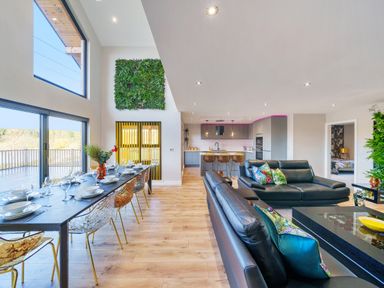 An open plan living room and kitchen with a dining table set with plates and glasses and black sofas with colorful cushions at Micklemore Lakes and Lodges North Thoresby