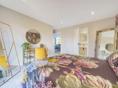 A bedroom with a floral bedspread a yellow chair a round mirror on a desk and a tall framed mirror at Micklemore Lakes and Lodges North Thoresby
