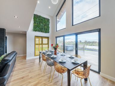 A dining area with a large table set for eight people and large windows overlooking a deck at Micklemore Lakes and Lodges in North Thoresby