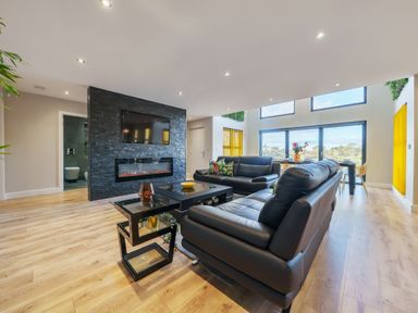 A living room with black leather sofas a black stone fireplace and a dining table near large windows at Micklemore Lakes and Lodges in North Thoresby