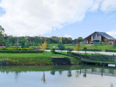 A lake with reflections of trees and a wooden house with a sloped roof at Micklemore Lakes and Lodges in North Thoresby