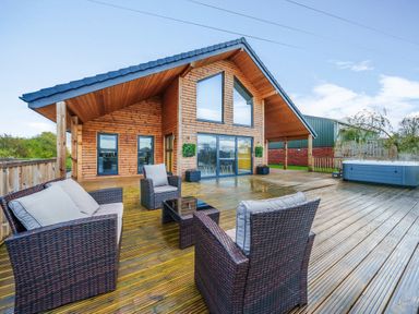 An outdoor wooden deck with wicker furniture and a hot tub at Micklemore Lakes and Lodges in North Thoresby