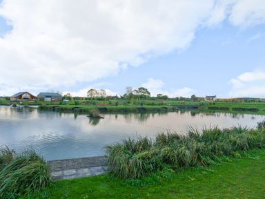 A lake with grassy banks and houses in the background at Micklemore Lakes and Lodges in North Thoresby