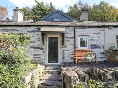 Stone cottage entrance with a wooden bench and plants at 4 Ty Person in Braichmelyn near Bethesda