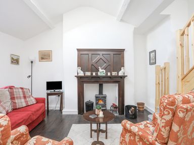 A living room with a fireplace a red sofa armchairs and a small table at 4 Ty Person in Braichmelyn near Bethesda