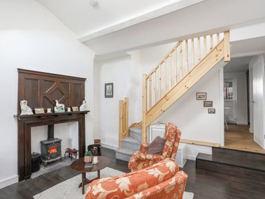 A living room with orange patterned armchairs a wooden staircase and a fireplace with decorative items at 4 Ty Person in Braichmelyn near Bethesda