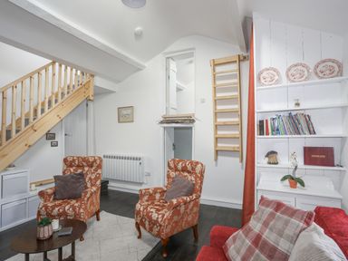 A living room with patterned armchairs and wooden staircase and shelves with books at 4 Ty Person in Braichmelyn near Bethesda