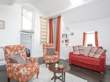 A living room with orange patterned armchairs a red sofa and a small round wooden table at 4 Ty Person in Braichmelyn near Bethesda
