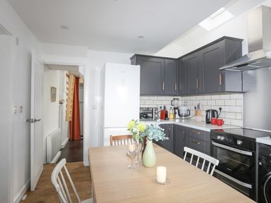 A kitchen with gray cabinets a white refrigerator a wooden dining table with chairs and a flower vase at 4 Ty Person in Braichmelyn near Bethesda
