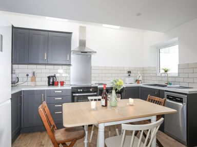 A kitchen with dark cabinets a wooden dining table with chairs and kitchen appliances at 4 Ty Person in Braichmelyn near Bethesda