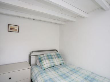 A small bedroom with a single bed with plaid bedding and pillow a white dresser and a small framed picture on the white wall at 4 Ty Person in Braichmelyn near Bethesda