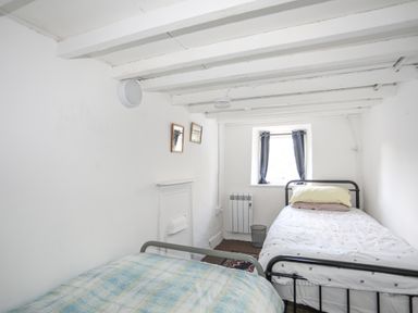A small bedroom with two single beds a window with curtains and a radiator at 4 Ty Person in Braichmelyn near Bethesda