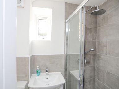 A bathroom with a sink and hand soap next to a shower with glass door and rainfall showerhead at 4 Ty Person in Braichmelyn near Bethesda