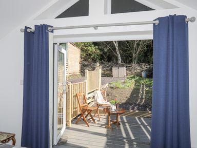 A patio with wooden chairs and a small table outside blue curtains at 4 Ty Person in Braichmelyn near Bethesda