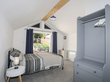 A bedroom with a bed side table lamp open door with curtains wardrobe and chest of drawers at 4 Ty Person in Braichmelyn near Bethesda