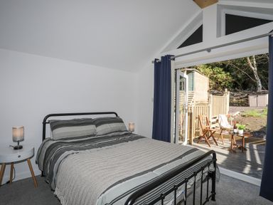 A bedroom with a double bed and two bedside lamps next to an open door leading to a small outdoor seating area at 4 Ty Person in Braichmelyn near Bethesda