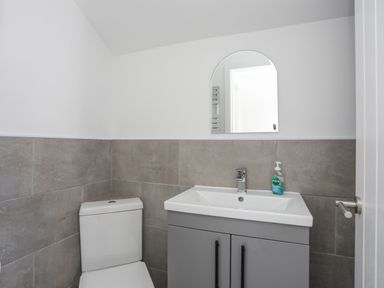 A bathroom with a toilet, sink with cabinet, mirror, and hand soap at 4 Ty Person in Braichmelyn near Bethesda
