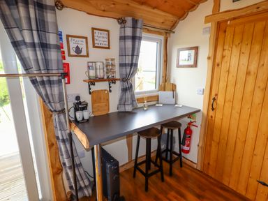 A small dining area with a counter table and two stools near a wooden door and window at Moel Y Parc in Bryniau Clwyd near Denbigh