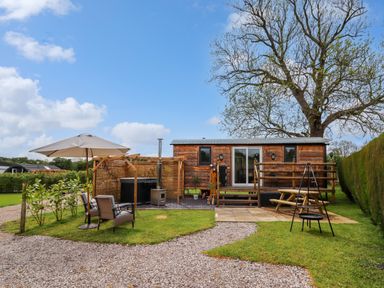 An outdoor area with a wooden cabin surrounded by grass and trees with patio furniture and a hot tub at Moel Y Parc in Bryniau Clwyd near Denbigh