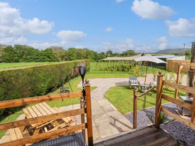 An outdoor garden area with wooden picnic table umbrella chairs and a patio at Moel Y Parc in Bryniau Clwyd near Denbigh