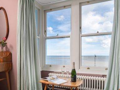 A window view with a table holding champagne and a magazine at Astondene, East Cliff Southwold