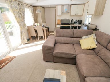 A living room with brown sectional sofa and dining table next to kitchen at 116 Woodpecker Lodge in Gilfachrheda near Llanarth