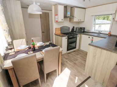 A kitchen and dining area with a table set for four and cabinets in a corner layout at 116 Woodpecker Lodge in Gilfachrheda near Llanarth
