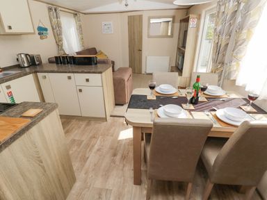 A dining area with a set table and kitchen with appliances in a small living space at 116 Woodpecker Lodge in Gilfachrheda near Llanarth
