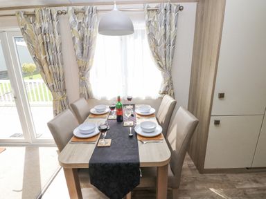 A dining area with a set table for four including wine glasses and bowls at 116 Woodpecker Lodge in Gilfachrheda near Llanarth